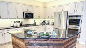 A modern kitchen with white cabinets, stainless steel appliances, a central island with a wooden base, and a glass countertop.
