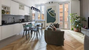 A modern kitchen with white cabinets, a dining area with a glass table and chairs, a sofa with cushions, and a large window with a city view. - Our apartment is in a building of the past century, it's on the 2nd floor and served by an elevator.You will have at your disposal 2 bedrooms, 2 bathrooms, and a living room, with a cooking area, that will be able to accommodate up to 5 people.The livi (Roma)