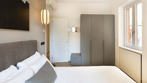 A modern hotel room with a large bed, a wardrobe, a bedside table, and a window. - Our apartment is in a building of the past century, it's on the 2nd floor and served by an elevator.You will have at your disposal 2 bedrooms, 2 bathrooms, and a living room, with a cooking area, that will be able to accommodate up to 5 people.The livi (Roma)