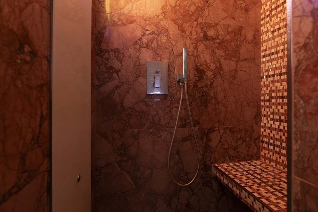 Ein Badezimmer mit Marmorwand, einer Dusche inklusive Handbrause und einer karierten Sitzbank.