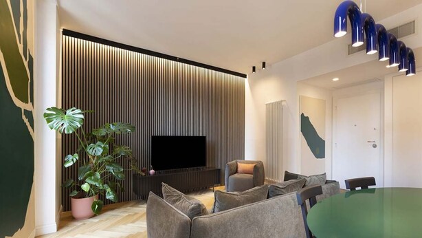 A modern living room with a large flat-screen TV, a grey sofa, a dining table, and a potted plant. - Our apartment is in a building of the past century, it's on the 2nd floor and served by an elevator.You will have at your disposal 2 bedrooms, 2 bathrooms, and a living room, with a cooking area, that will be able to accommodate up to 5 people.The livi (Roma)