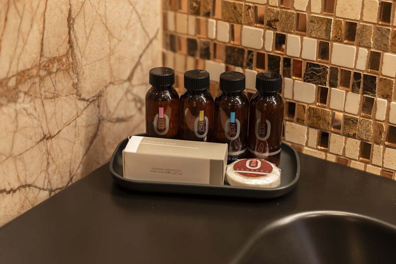 A tray with four brown bottles, a white box, and a black bowl on a black countertop against a tiled wall.