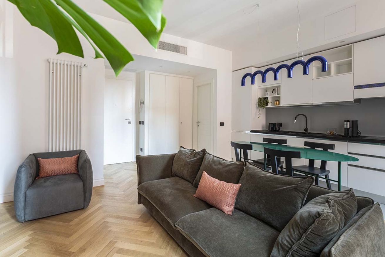 A modern living room with a grey sofa, a small armchair, and a dining table with chairs.