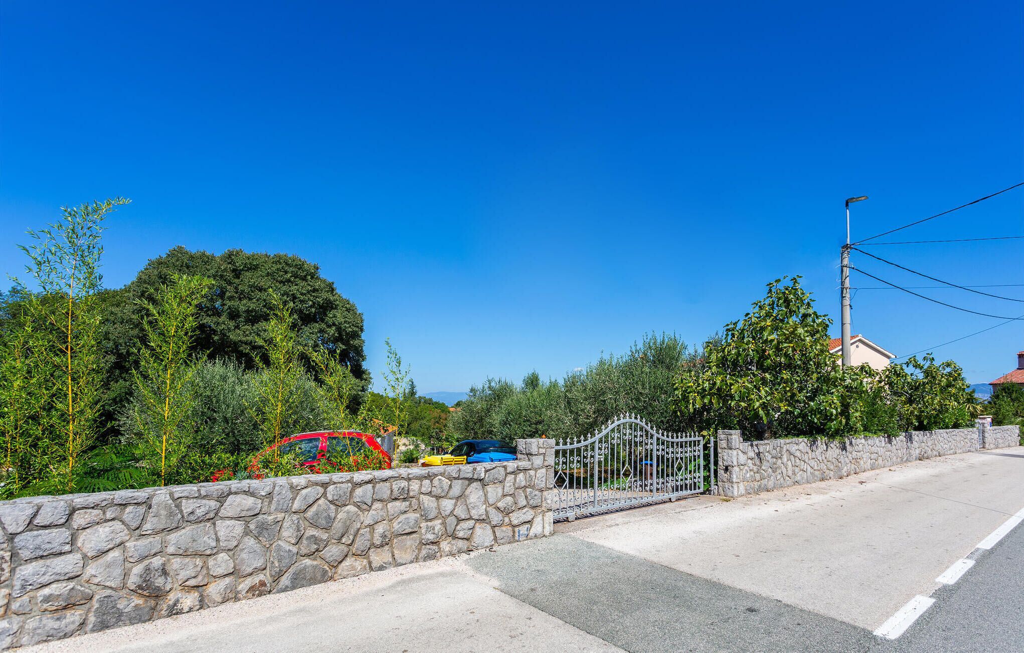 A stone wall with a metal gate, a road, and parked cars.