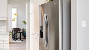 A modern kitchen with a stainless steel refrigerator, white cabinetry, and a wooden dining table with chairs. - Spacious Las Vegas Home Near Casinos & Nightlife! (Las Vegas)