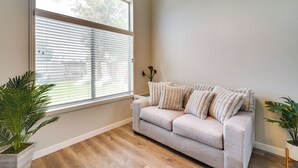 A room with a beige sofa, a large window with blinds, a potted plant, and a wooden floor. - Spacious Las Vegas Home Near Casinos & Nightlife! (Las Vegas)