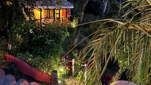 Un jardín con una estructura de madera, rodeado de abundante vegetación y un sendero de piedra.