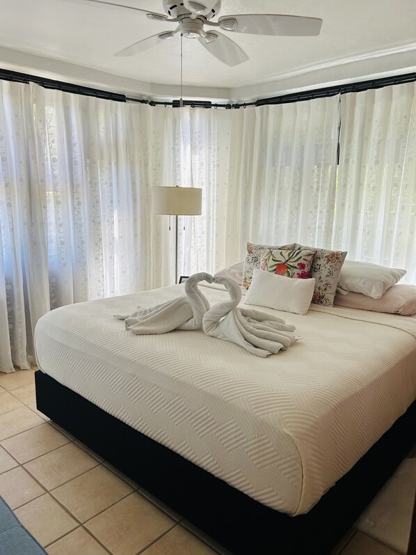 Una cama bien hecha con un arreglo decorativo de toallas, un ventilador de techo y una lámpara de pie.