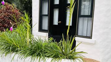 Un edificio bianco con una porta e finestre nere, circondato da piante verdi e un piccolo giardino.
