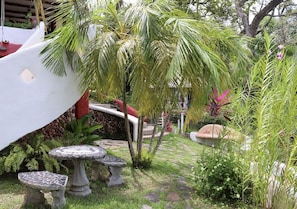 Un jardín con palmeras, un sendero de piedra y una estructura blanca con techo rojo.