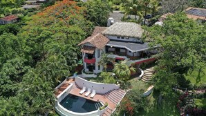 Una amplia casa con piscina, rodeada de exuberante follaje y palmeras.