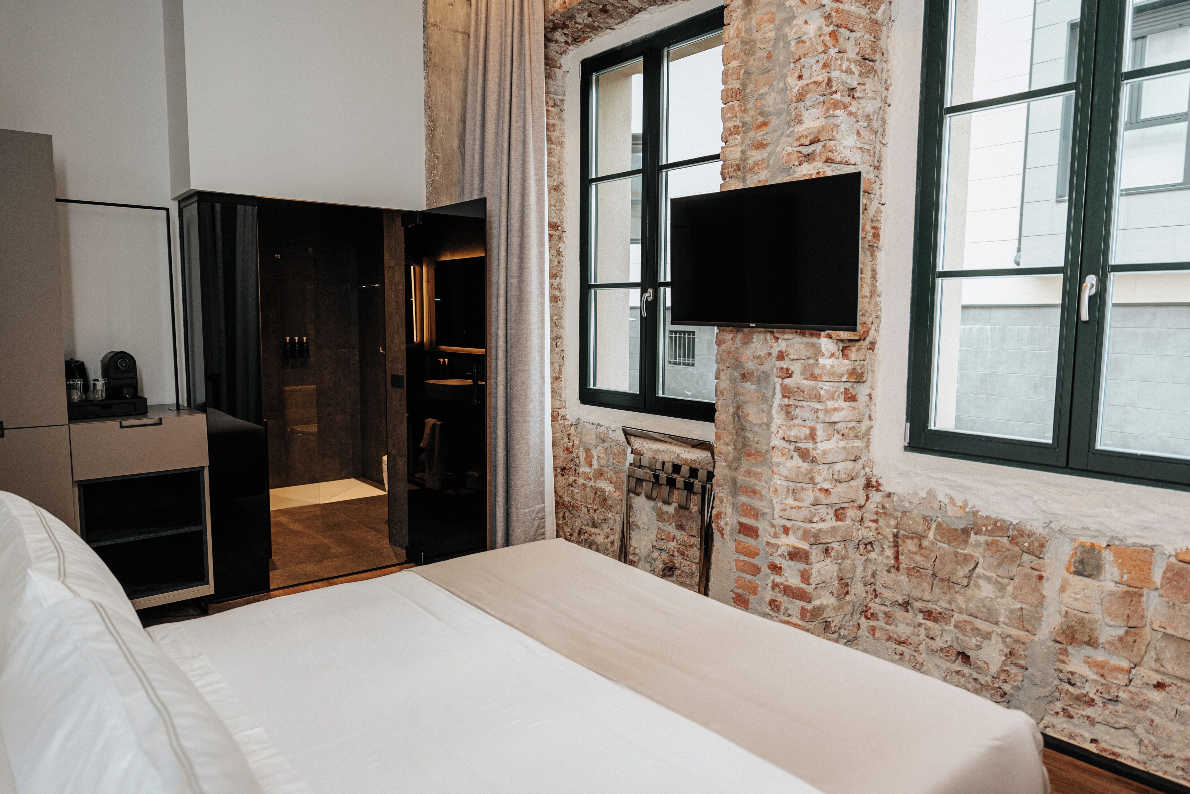 Hotelkamer met een groot bed, een televisie bevestigd aan een bakstenen muur en een raam met uitzicht op de stad.