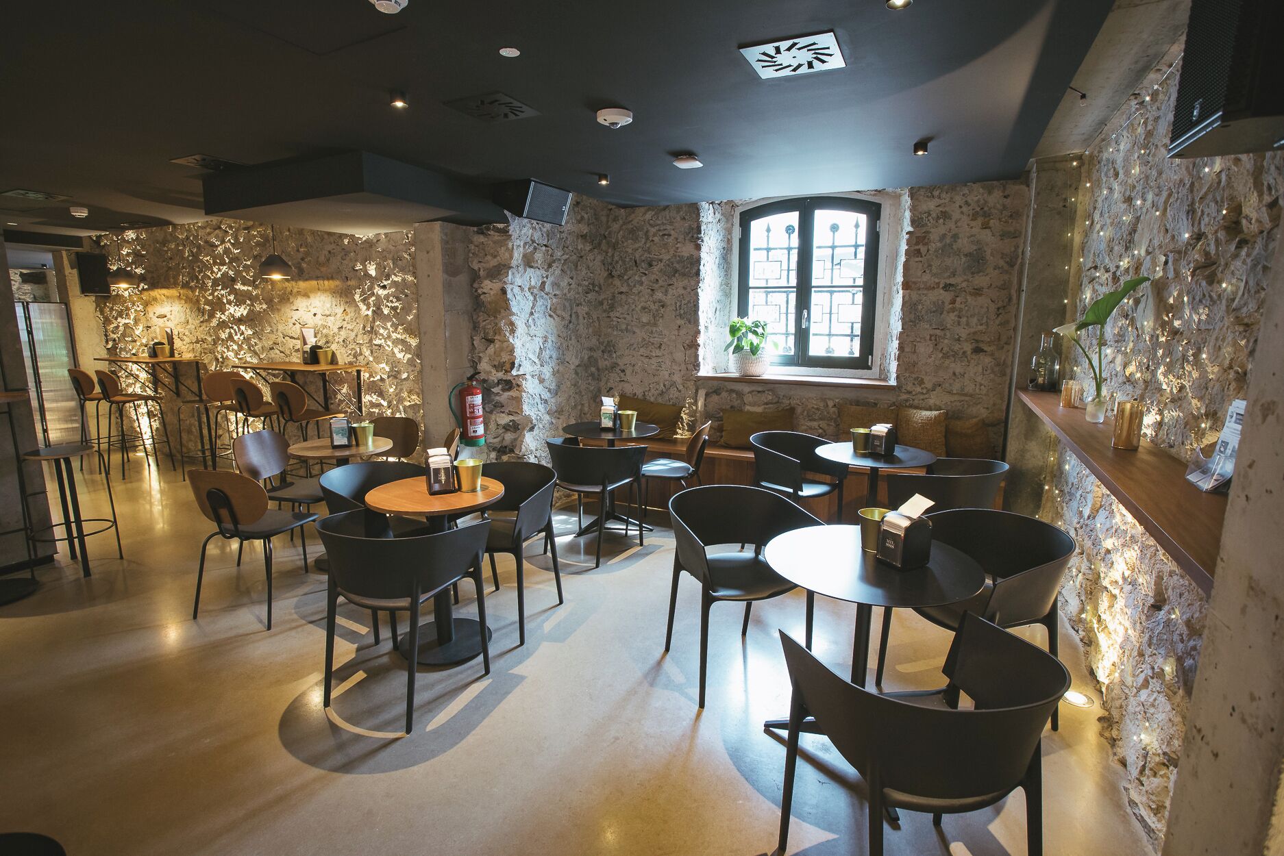 A restaurant with stone walls, round tables, and black chairs.