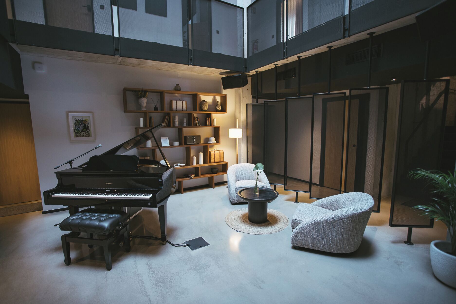 Un vaste salon agrémenté d’un magnifique piano à queue, d’un fauteuil confortable, d’une table basse ronde et d’une bibliothèque remplie de divers objets.