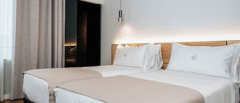 Una camera d'albergo con due letti, una testiera in legno, un lampadario e vista sull'esterno attraverso una finestra con tende.