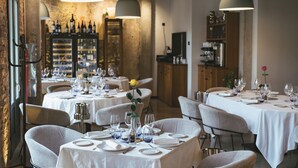Ein Restaurantinneres mit runden Tischen, gedeckt für das Essen, mit weißen Tischdecken und einer Auswahl an Weinflaschen und -gläsern auf Regalen im Hintergrund.
