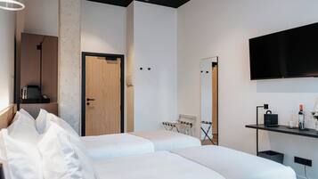 A modern hotel room with two beds, a large mirror, a flat-screen TV, and a small desk with a coffee machine.