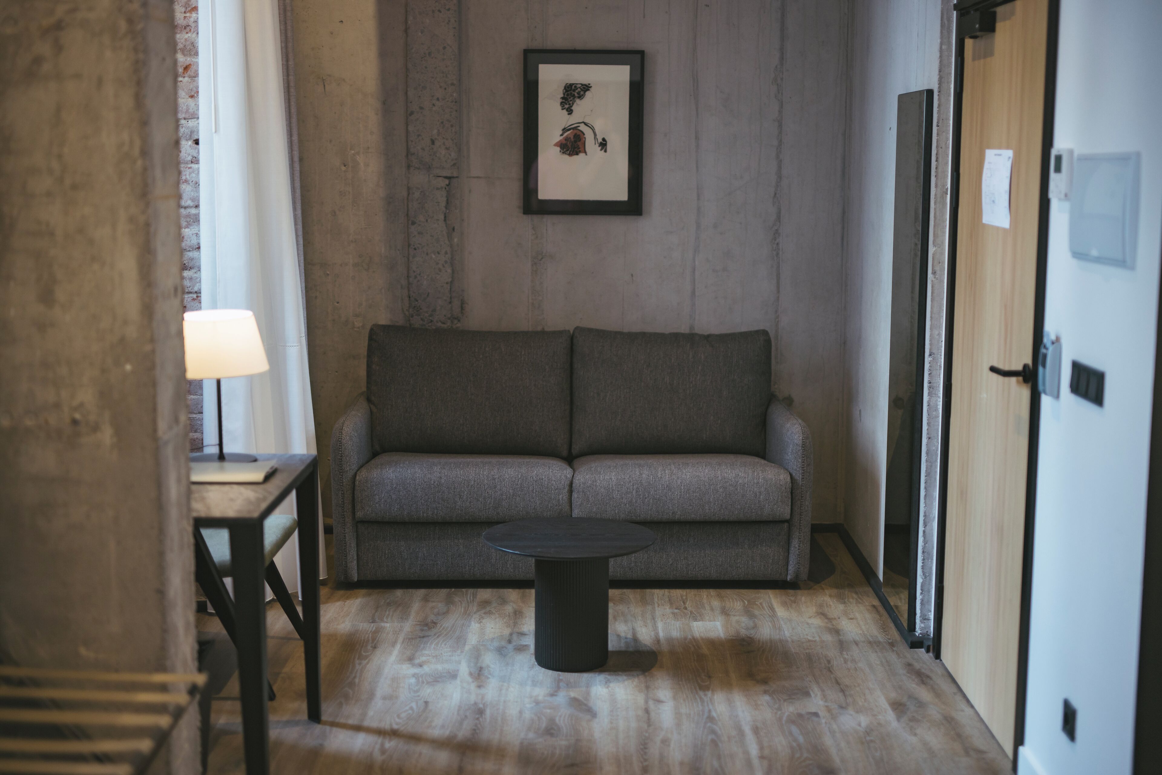 A room with a grey sofa, a round black table, and a framed picture on the wall.
