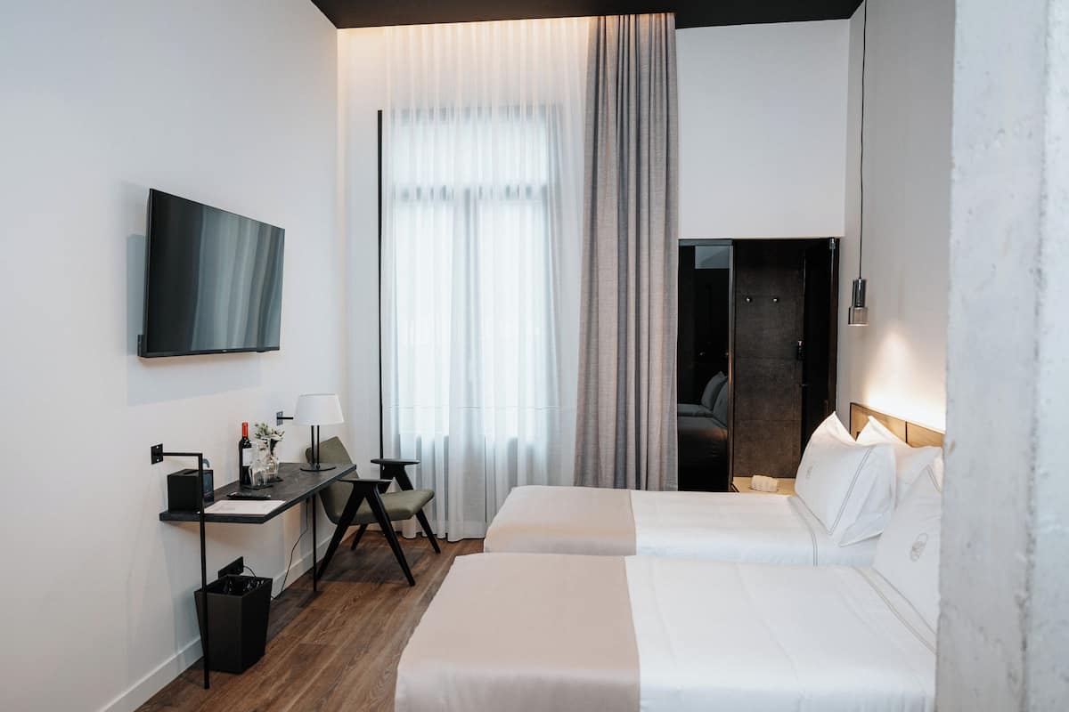A hotel room with a bed, a desk, a chair, a TV, and a window with curtains.