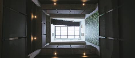 A modern interior with a central staircase leading to a bright room with a large window.