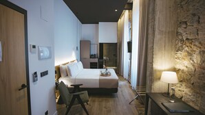 A modern hotel room with a bed, bedside table, chair, and a stone accent wall. - Hotel Luruna Palacio Larrinaga  (Mundaka)