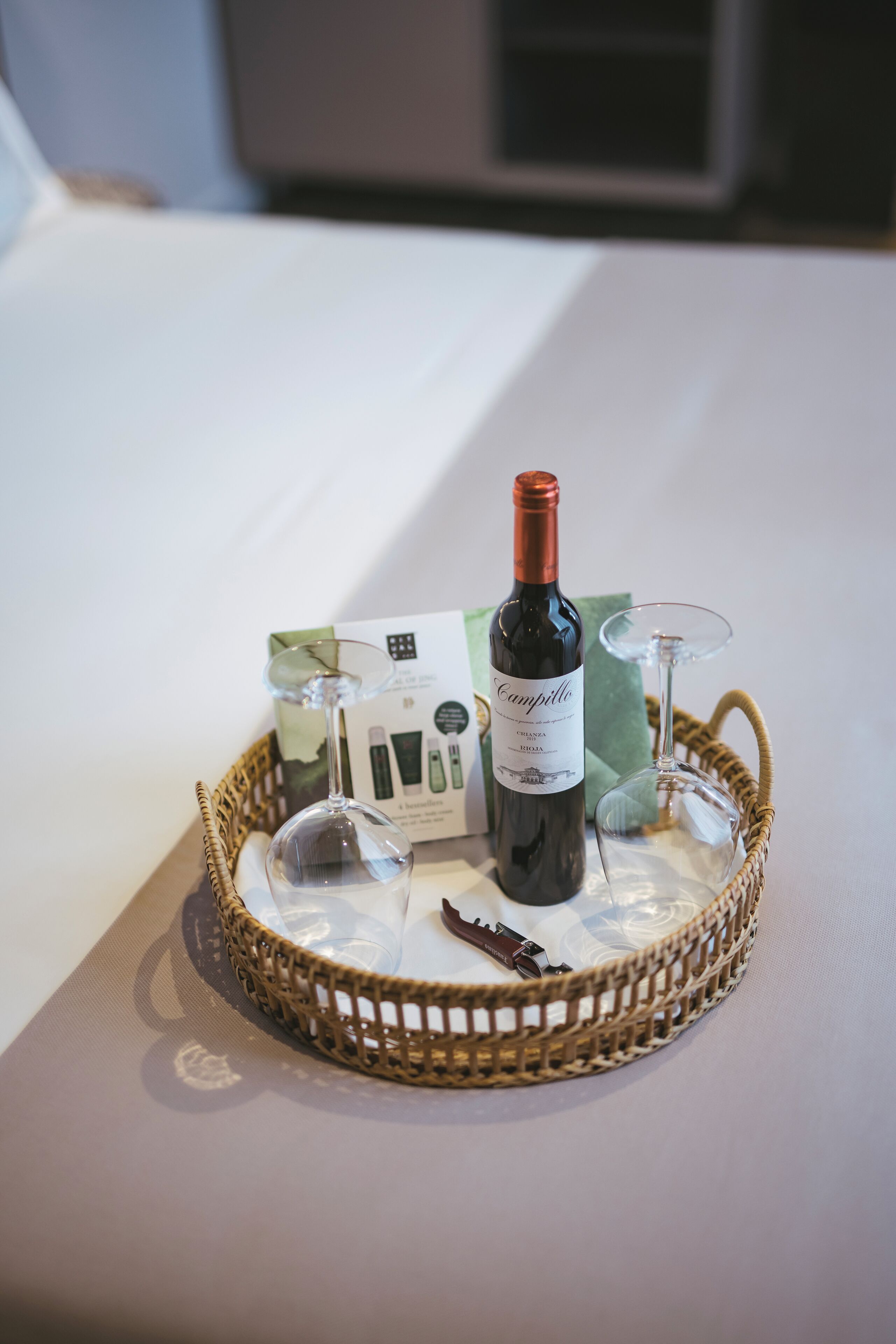 A wicker basket with a wine bottle and two wine glasses on a table.