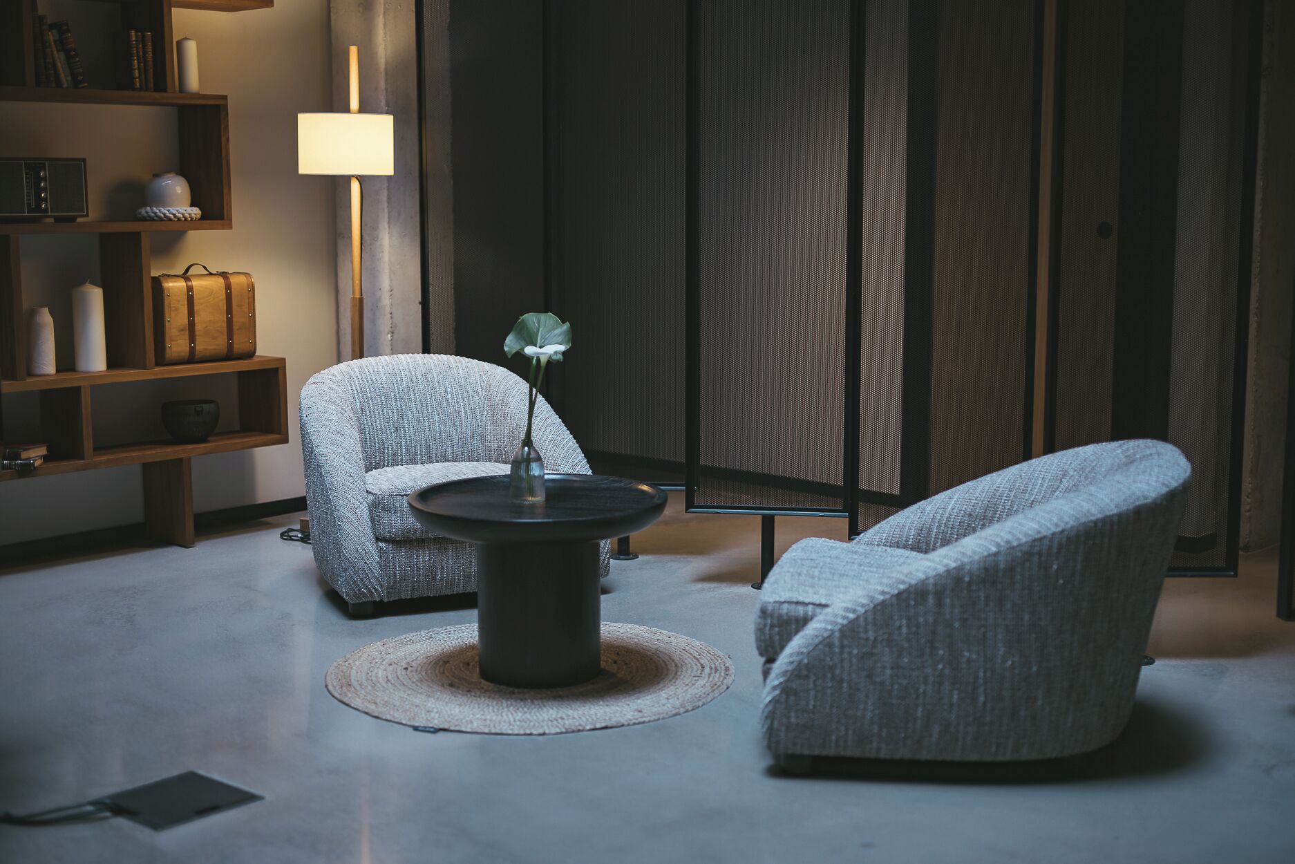 A modern living room with two grey upholstered chairs, a round coffee table, and a bookshelf.
