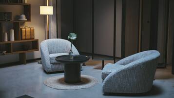 Una sala de estar moderna con dos sillones grises tapizados, una mesa redonda y una estantería.