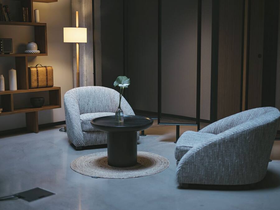 Una sala de estar moderna con dos sillones grises tapizados, una mesa redonda y una estantería.