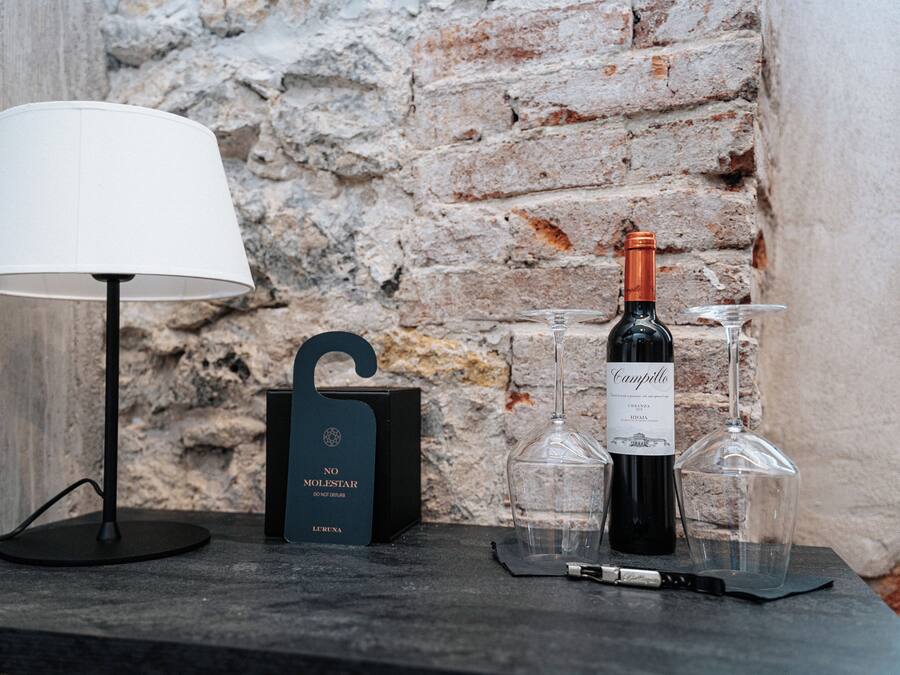 A table with a lamp, a wine bottle, wine glasses, and a box labeled "NO MOLESTAR".
