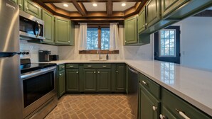 A kitchen with green cabinets, stainless steel appliances, and a herringbone floor pattern. - NEW OUTDOOR HOT TUB! Luxury 2 Bedroom Suite -The Haüs Windham (Windham)