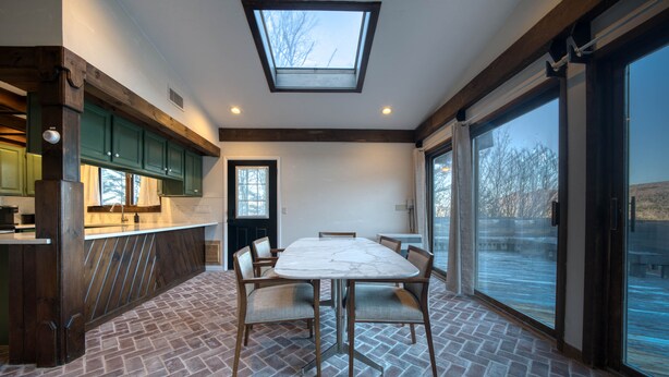 A dining area with a large table and chairs, a skylight, and a view of the outdoors. - NEW OUTDOOR HOT TUB! Luxury 2 Bedroom Suite -The Haüs Windham (Windham)