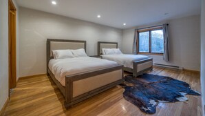 A bedroom with two beds, wooden flooring, a large window, and a fur rug. - NEW OUTDOOR HOT TUB! Luxury 2 Bedroom Suite -The Haüs Windham (Windham)