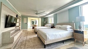 Un dormitorio amplio con una cama grande, un televisor montado en la pared, un escritorio con una silla y vista a la ciudad desde la ventana.