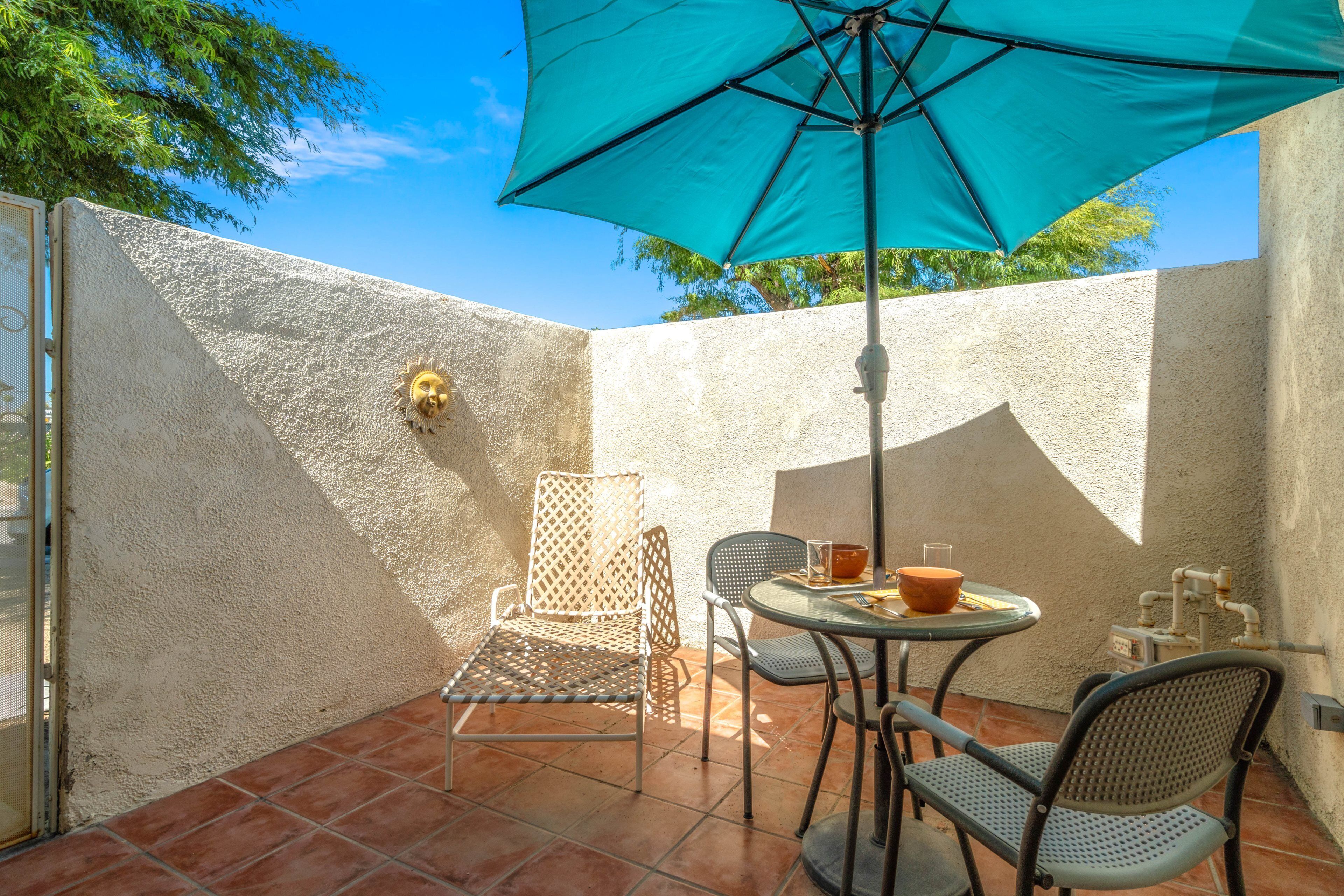 A patio with a table, chairs, a blue umbrella, and a decorative wall.
