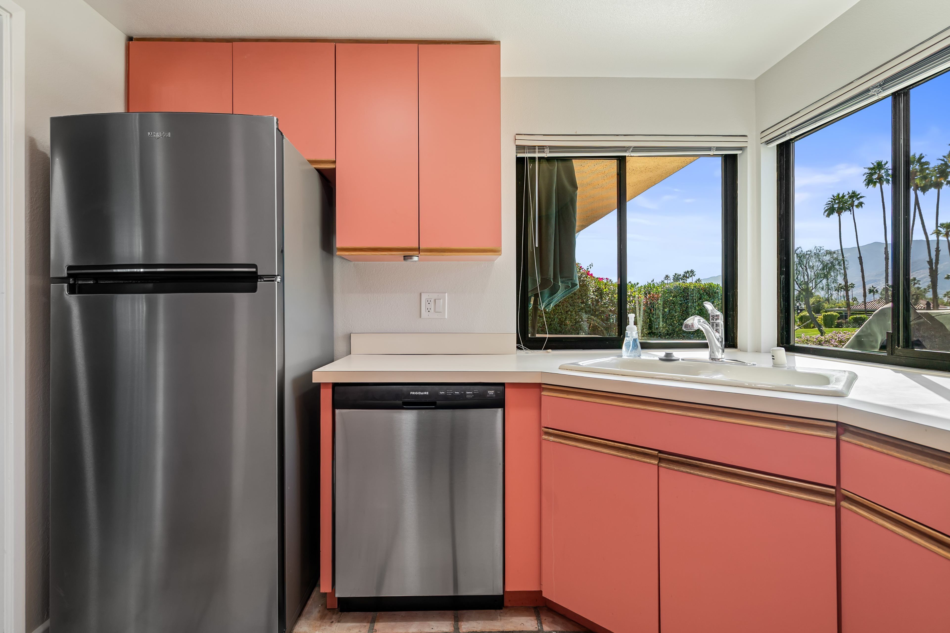 A kitchen with a stainless steel refrigerator, a dishwasher, and peach-colored cabinets.