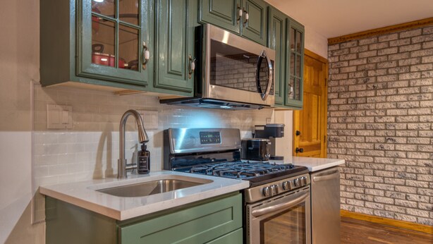 Une cuisine avec des meubles de couleur verte, une cuisinière en acier inoxydable et un four à micro-ondes.
