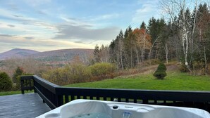 Un bain à remous sur une terrasse en bois, avec vue sur une forêt et des montagnes.