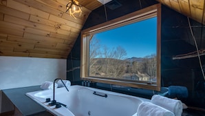 A wooden cabin with a large window, a bathtub, and towels. - PRESIDENTIAL DUPLEX SUITE WITH HOT TUB AND WRANP AROUND BALCONY (Windham)