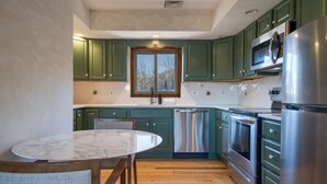 A kitchen with green cabinets, stainless steel appliances, a marble countertop, and a window above the sink. - PRESIDENTIAL DUPLEX SUITE WITH HOT TUB AND WRANP AROUND BALCONY (Windham)