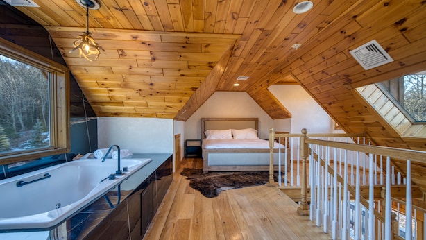 A bedroom with a wooden ceiling, a large window, a bed, and a bathroom with a sink and mirror. - PRESIDENTIAL DUPLEX SUITE WITH HOT TUB AND WRANP AROUND BALCONY (Windham)