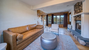 A modern living room with a brown leather sofa, a round ottoman, and a stone fireplace. - PRESIDENTIAL DUPLEX SUITE WITH HOT TUB AND WRANP AROUND BALCONY (Windham)