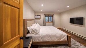 Un dormitorio con cama de madera, un televisor de pantalla plana en la pared, una ventana con cortinas y una lámpara de techo.