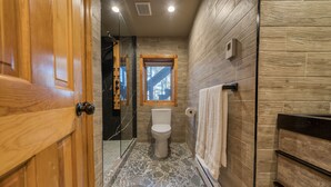Un baño con suelo de piedra, paredes de madera, un inodoro, una ventana y un perchero para toallas.