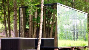 A modern, rectangular structure with a reflective glass facade, situated in a forested area.