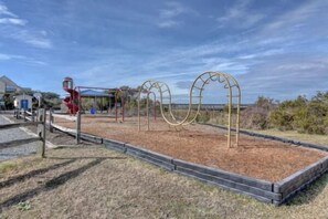 A playground with a red slide and swings, surrounded by a fenced area with mulch.