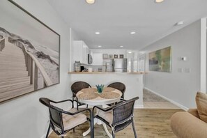 A dining area with a round table and chairs, a kitchen in the background, and a living room with a sofa. - 3 bdr, Oceanview, Pool, Private Beach access (Surf City)