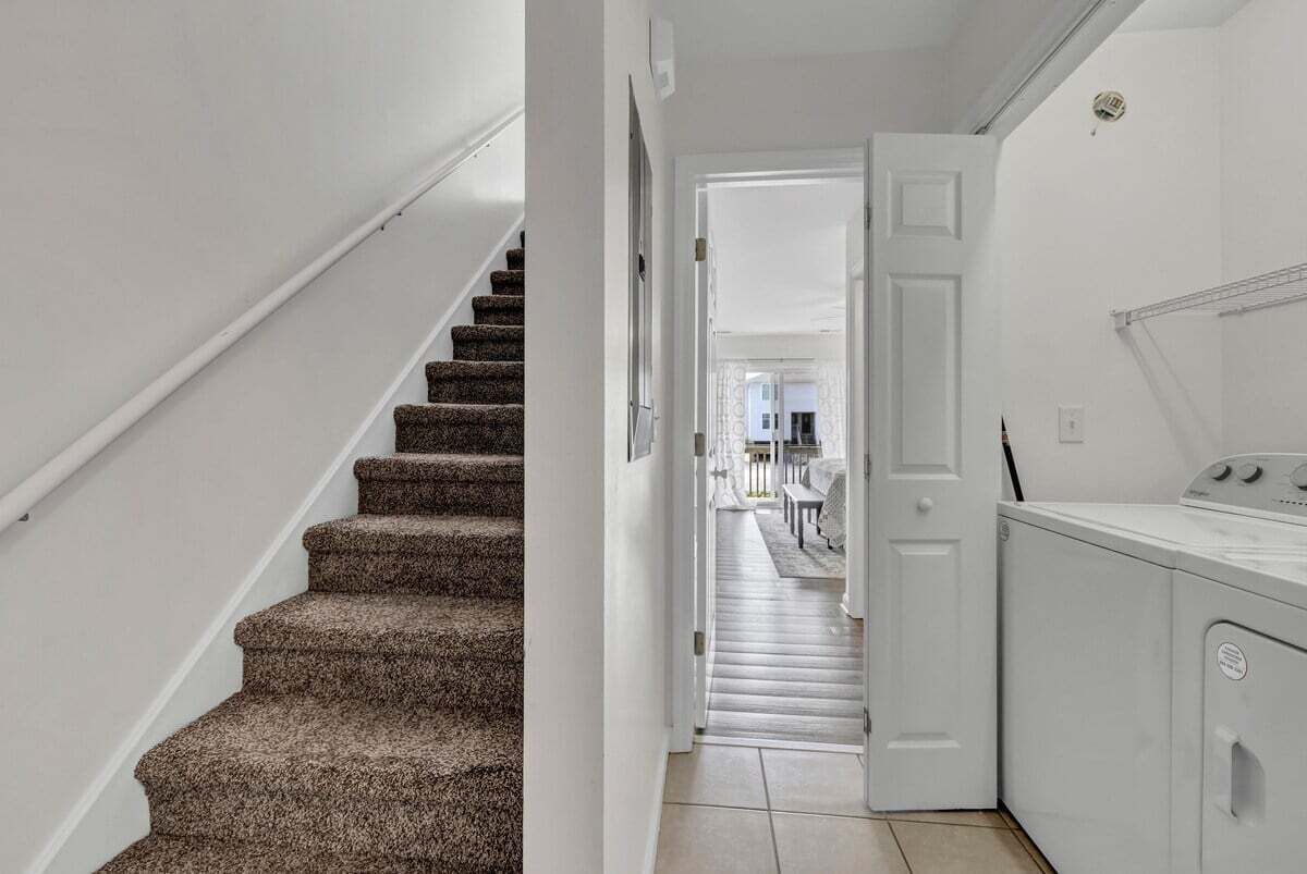 Una escalera conduce a un área de lavandería con una puerta blanca y una lavadora.