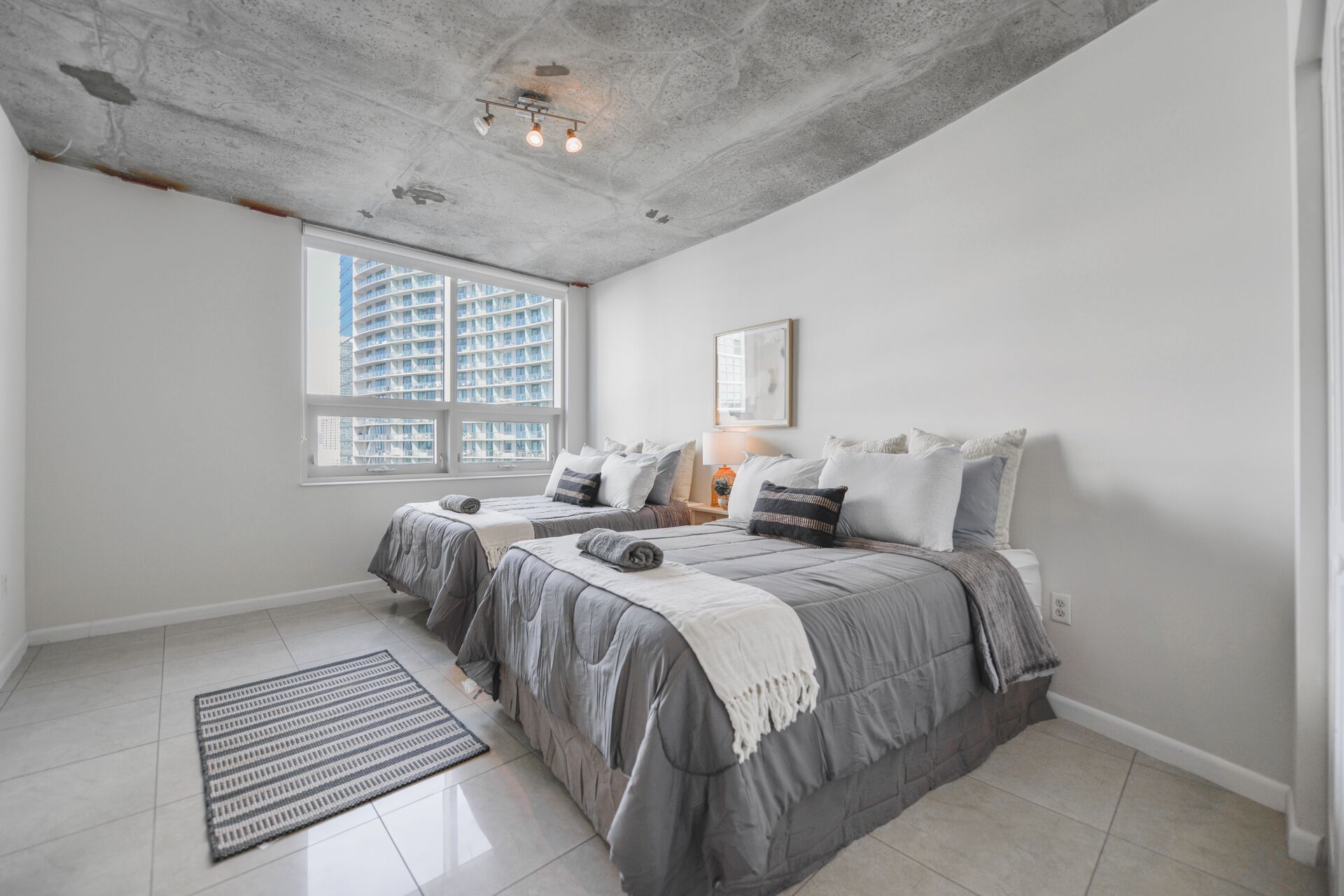 A bedroom with two beds, a large window, and a concrete ceiling.