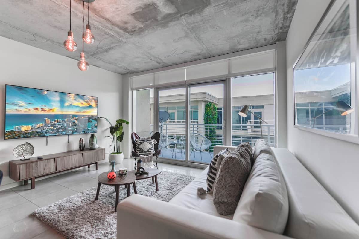 A modern living room with a large window, a sofa, a coffee table, and a painting of a cityscape.